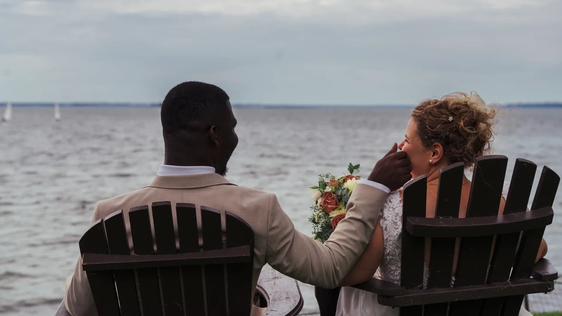 Les mariés assis de dos face à la mer, un bouquet à la main